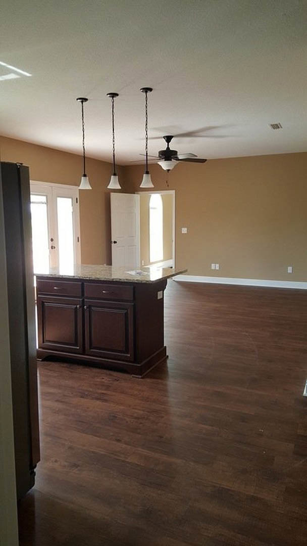 Open kitchen and dining area featuring marble countertops, hardwood flooring, white cabinetry, ceiling fan, and a white door adjacent to a metal post