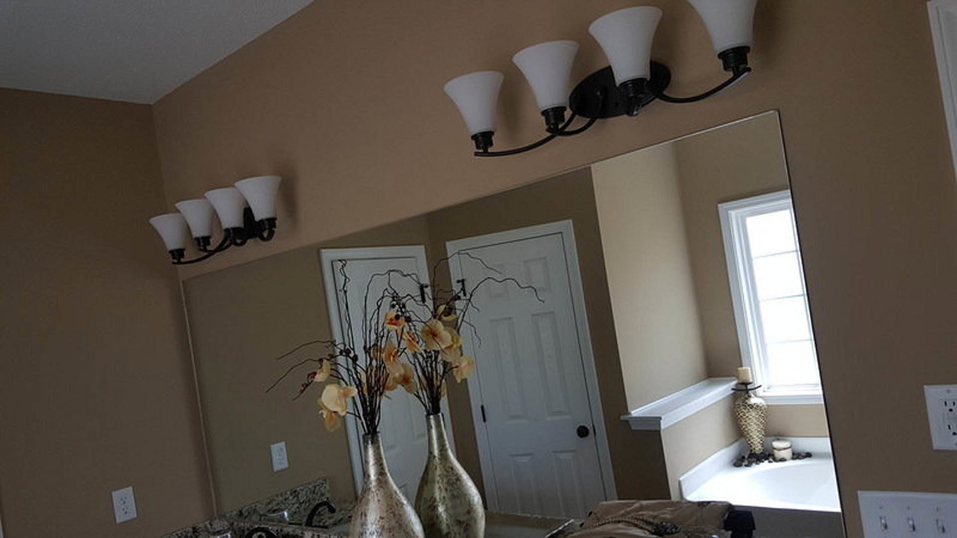 White plaster bathroom with rectangular mirror above a marble sink, chrome faucet, and vase of fresh flowers on the countertop