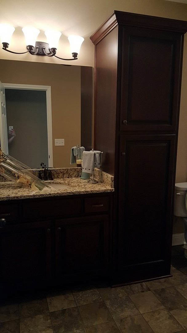 Modern bathroom featuring a white porcelain sink with chrome faucet, matching toilet, light gray tile flooring, wood cabinetry with drawers, and stone countertop against neutral
