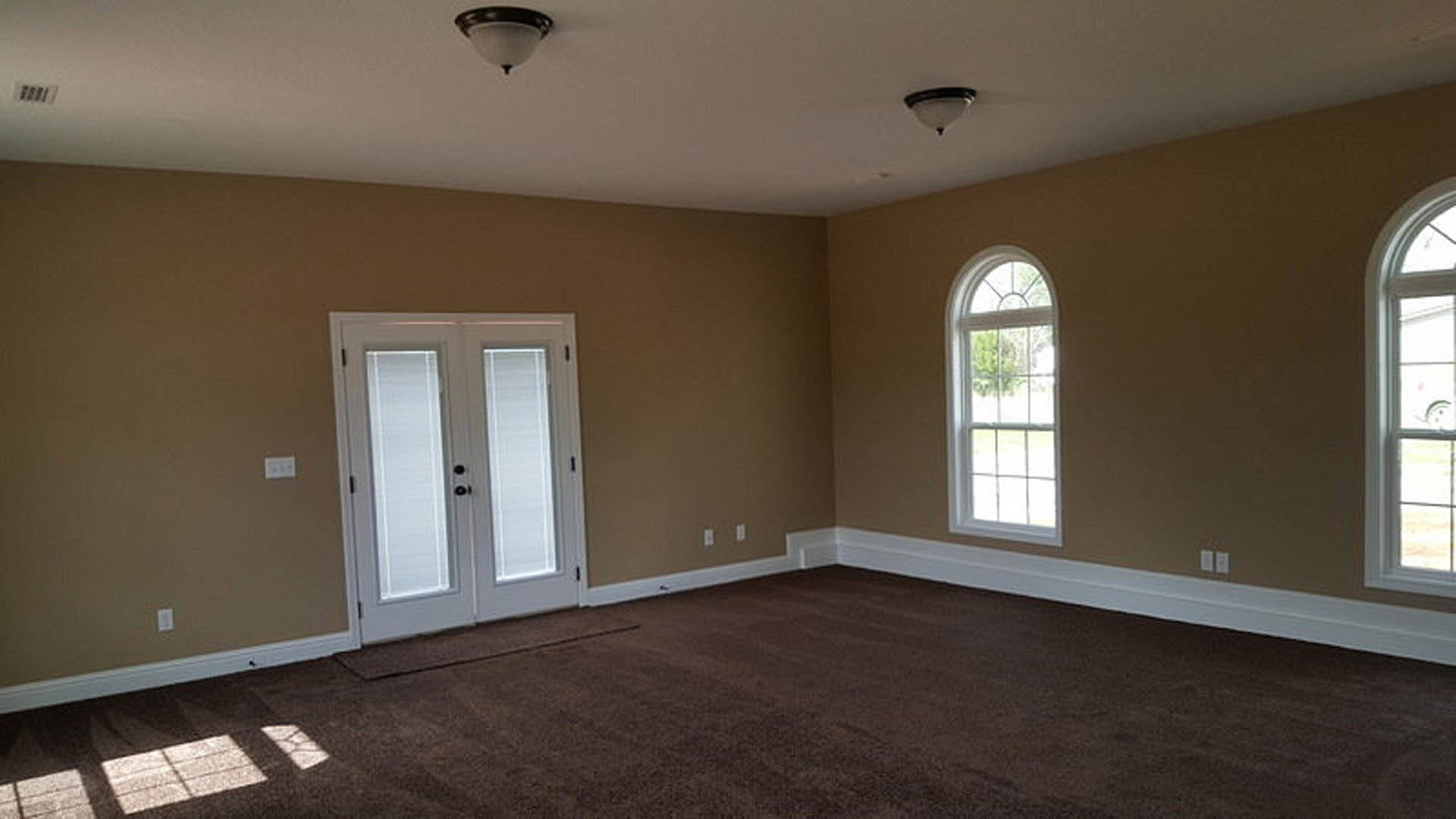 Bright room with white framed windows, double doors with built-in blinds, white square tile flooring, dark baseboards, and recessed ceiling lights
