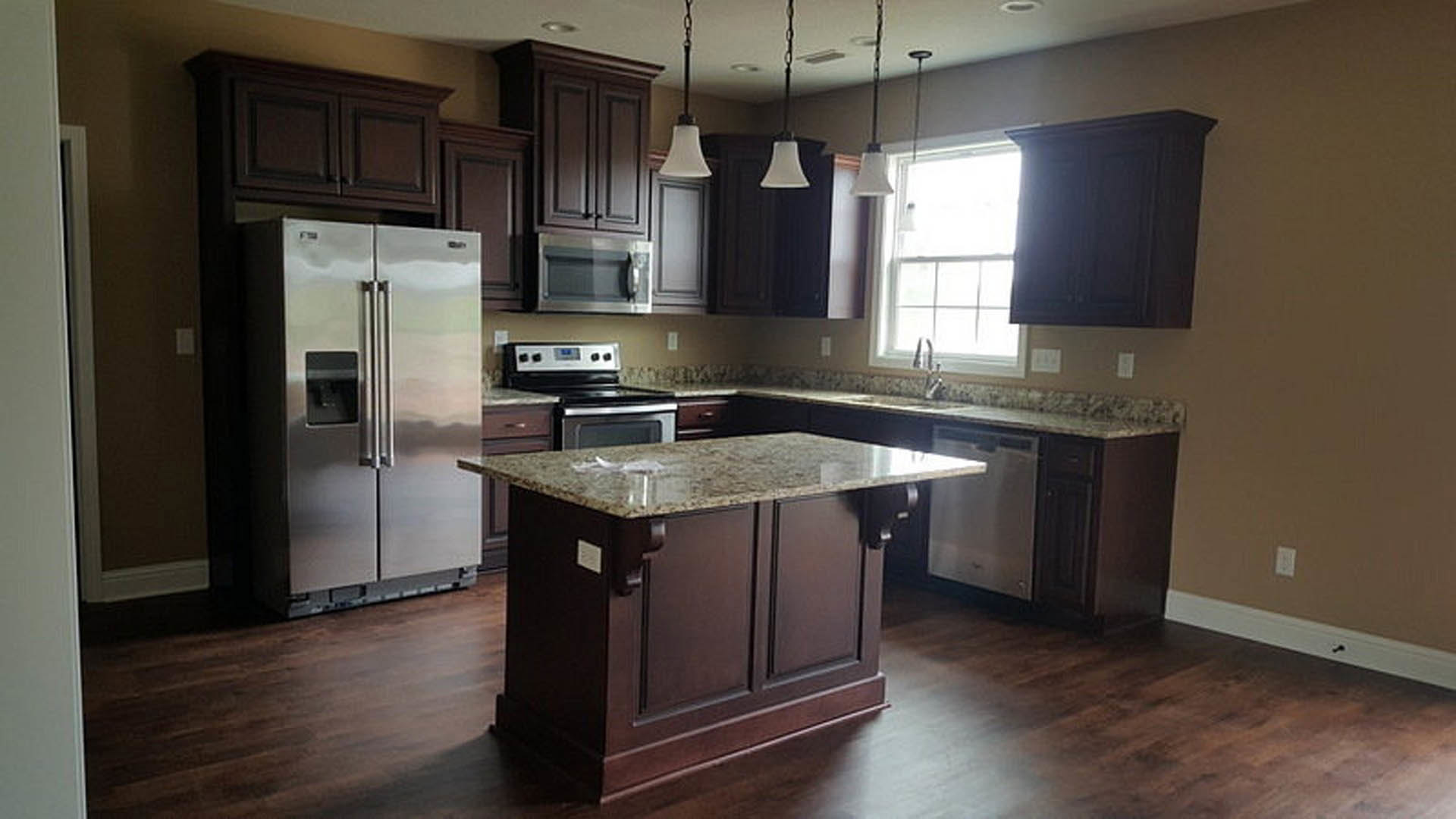 Spacious kitchen featuring a marble-topped island, stainless steel refrigerator, stove, microwave, white cabinetry, and sunlight streaming through a window