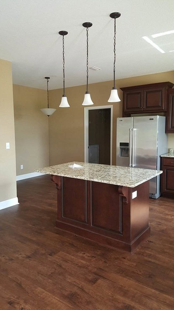 Marble-topped kitchen island with pendant lights, stainless steel refrigerator, white door frame, and cabinetry against neutral walls
