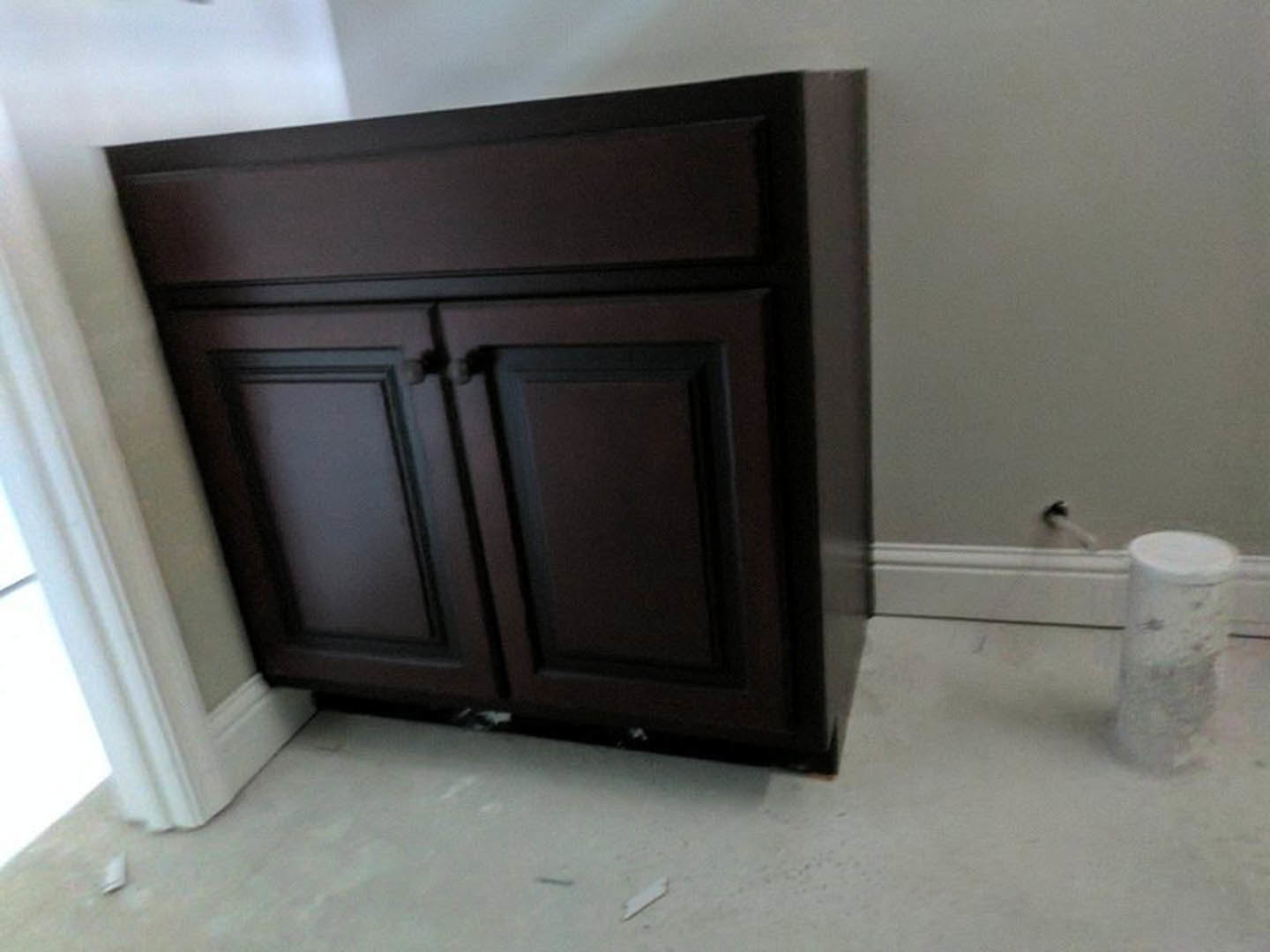 Dark brown bathroom cabinet with white countertop, tile flooring, and partial view of toilet and wall accessories