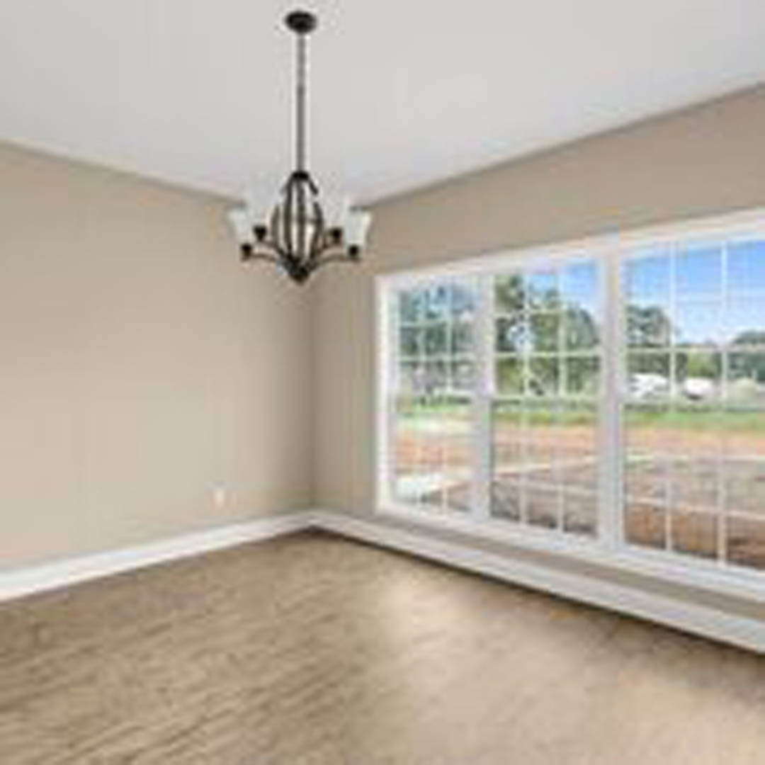 Spacious room featuring a large window with white trim, brown wood flooring, and neutral walls; natural light fills the space.