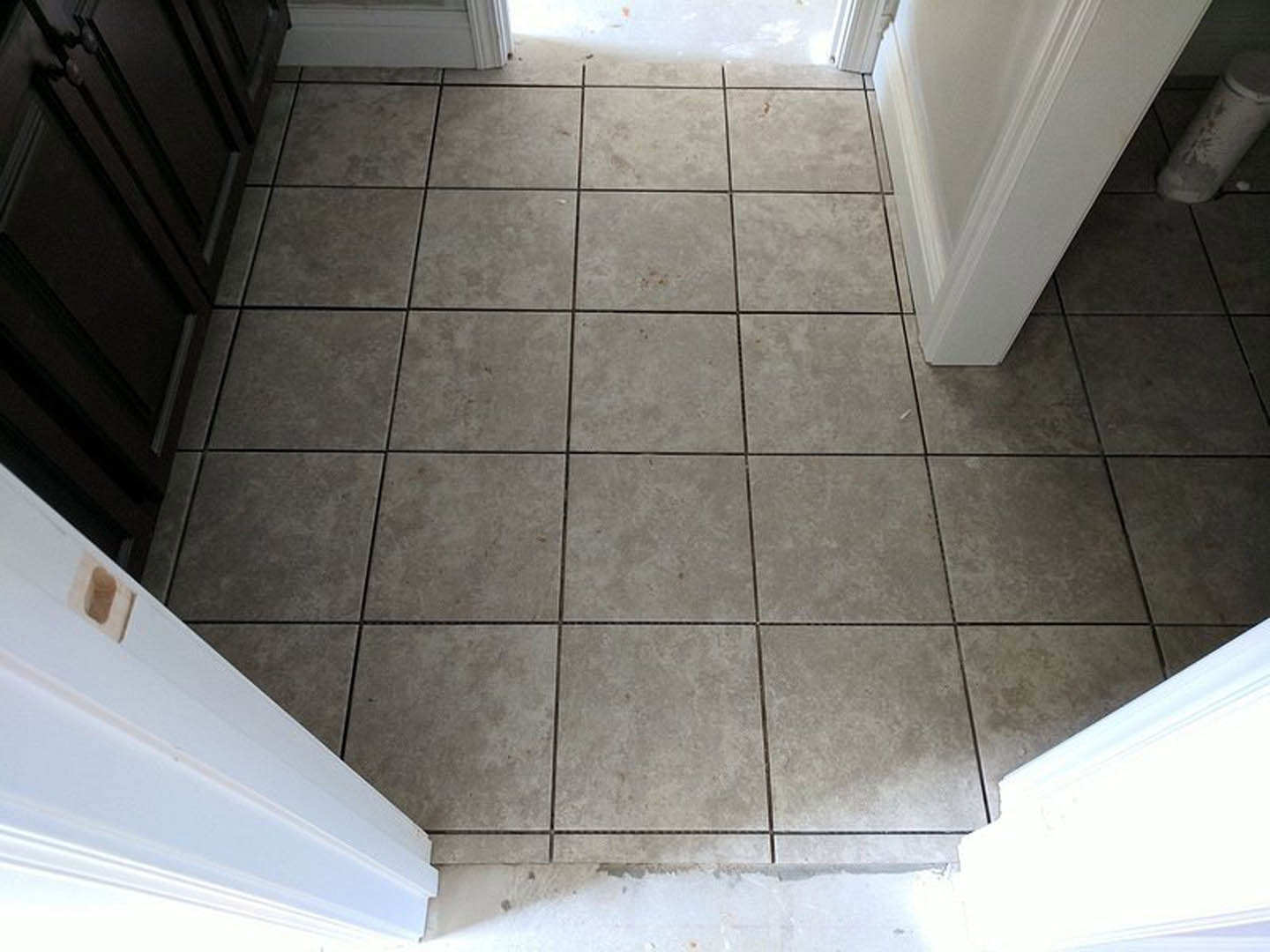 Tile floor with white grout and trim, white wall corner, white door with brown spot, cloudy sky visible through window