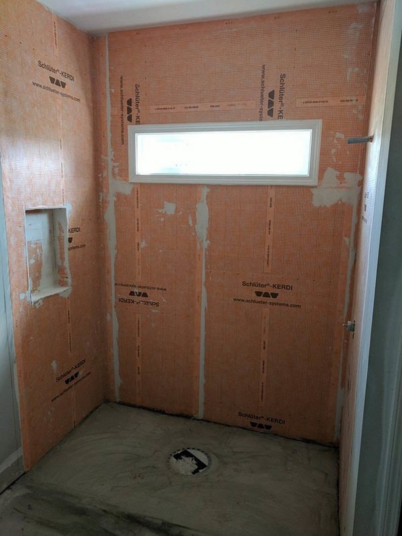 Bathroom with a large window set in a brick wall, walk-in shower area, exposed concrete floor, white trim, and unfinished surfaces.