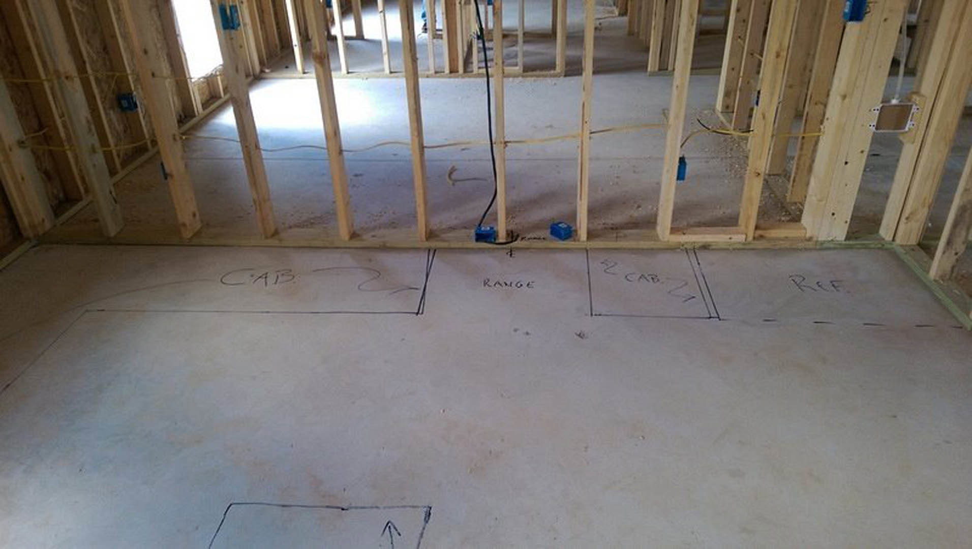 Unfinished room with exposed wood framing, electrical wiring, blue electrical boxes, and a whiteboard with writing