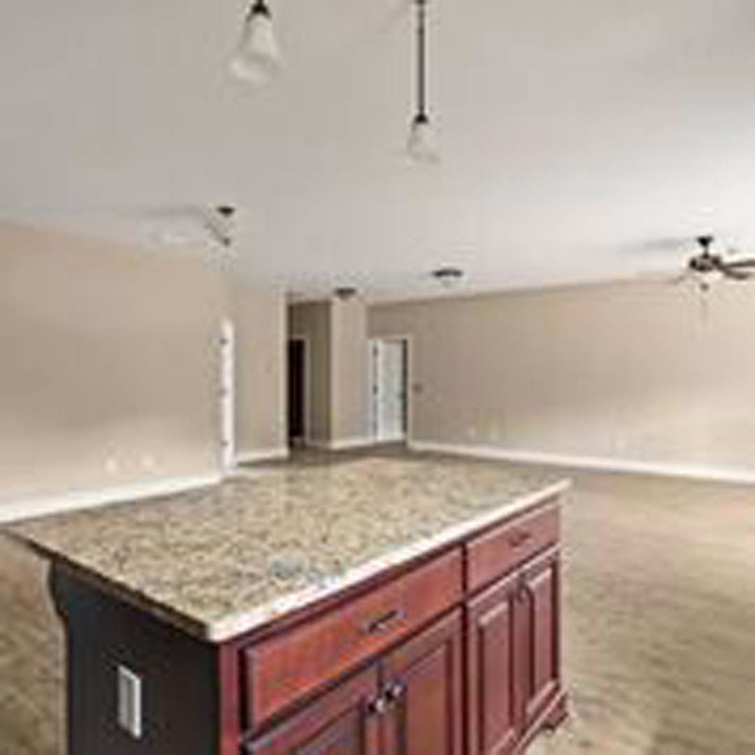 Marble kitchen island with white cabinetry, pendant lights overhead, stainless steel sink, tiled backsplash, and hardwood flooring