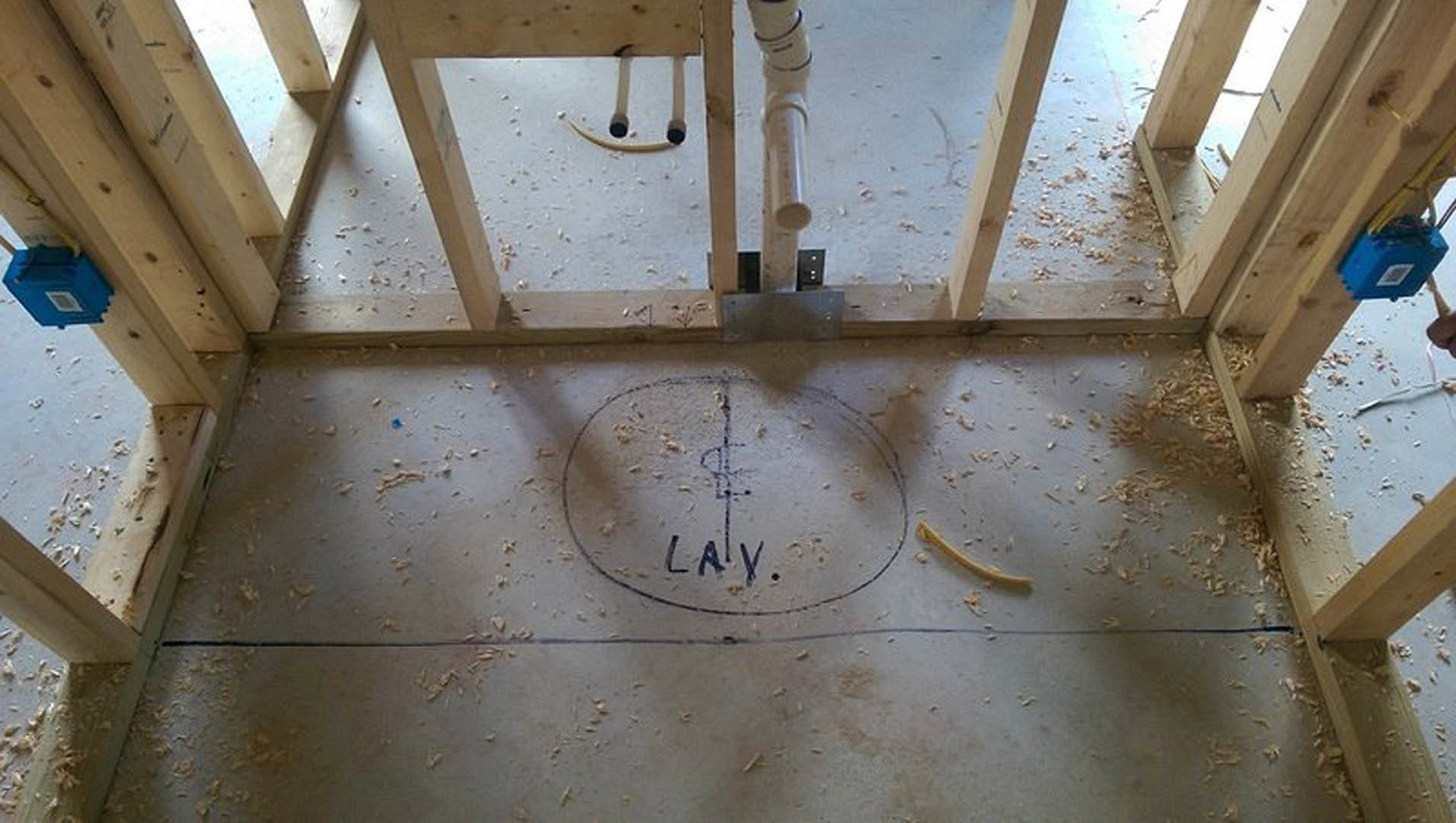 Exposed wood subfloor with a circular hole, visible insulation beneath, surrounded by unfinished beams in an indoor construction area