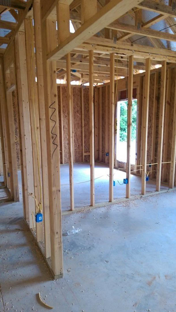 Unfinished room with exposed wood framing, ceiling beams, electrical wiring, and a window letting in natural light