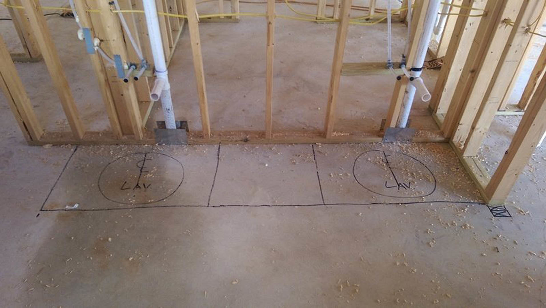 Hand-drawn circular sketch with writing on white floor surface, surrounded by unfinished wood framing in a residential interior under construction.