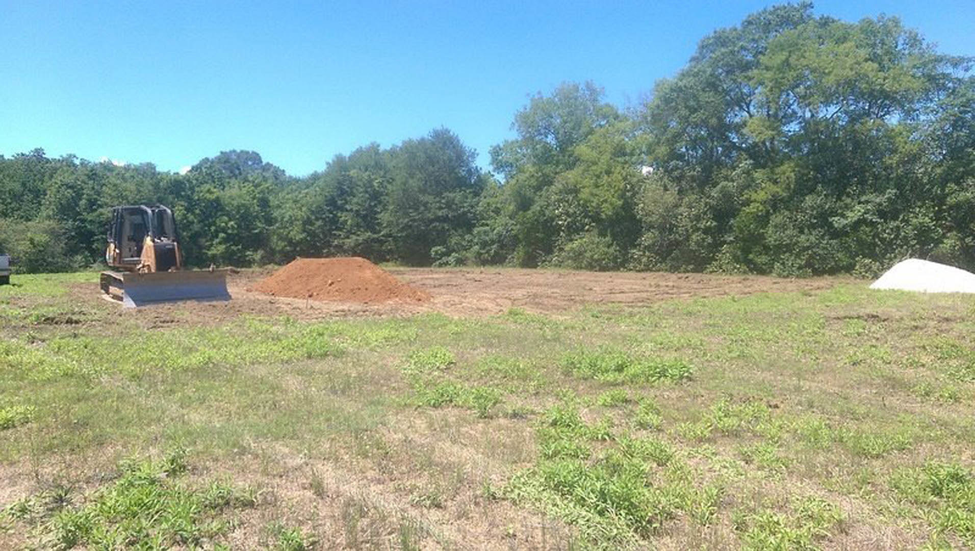 Dirt pile on grassy field with scattered trees and open sky in rural area