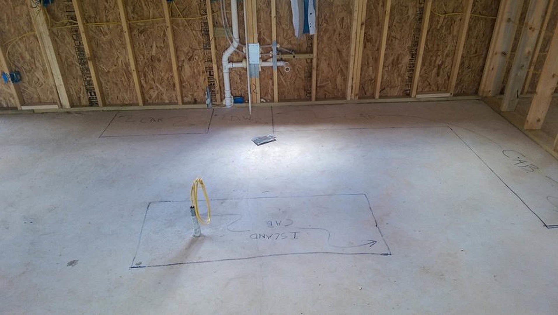 Concrete subfloor with hand-drawn construction markings, exposed yellow pipe, and white material in unfinished interior room