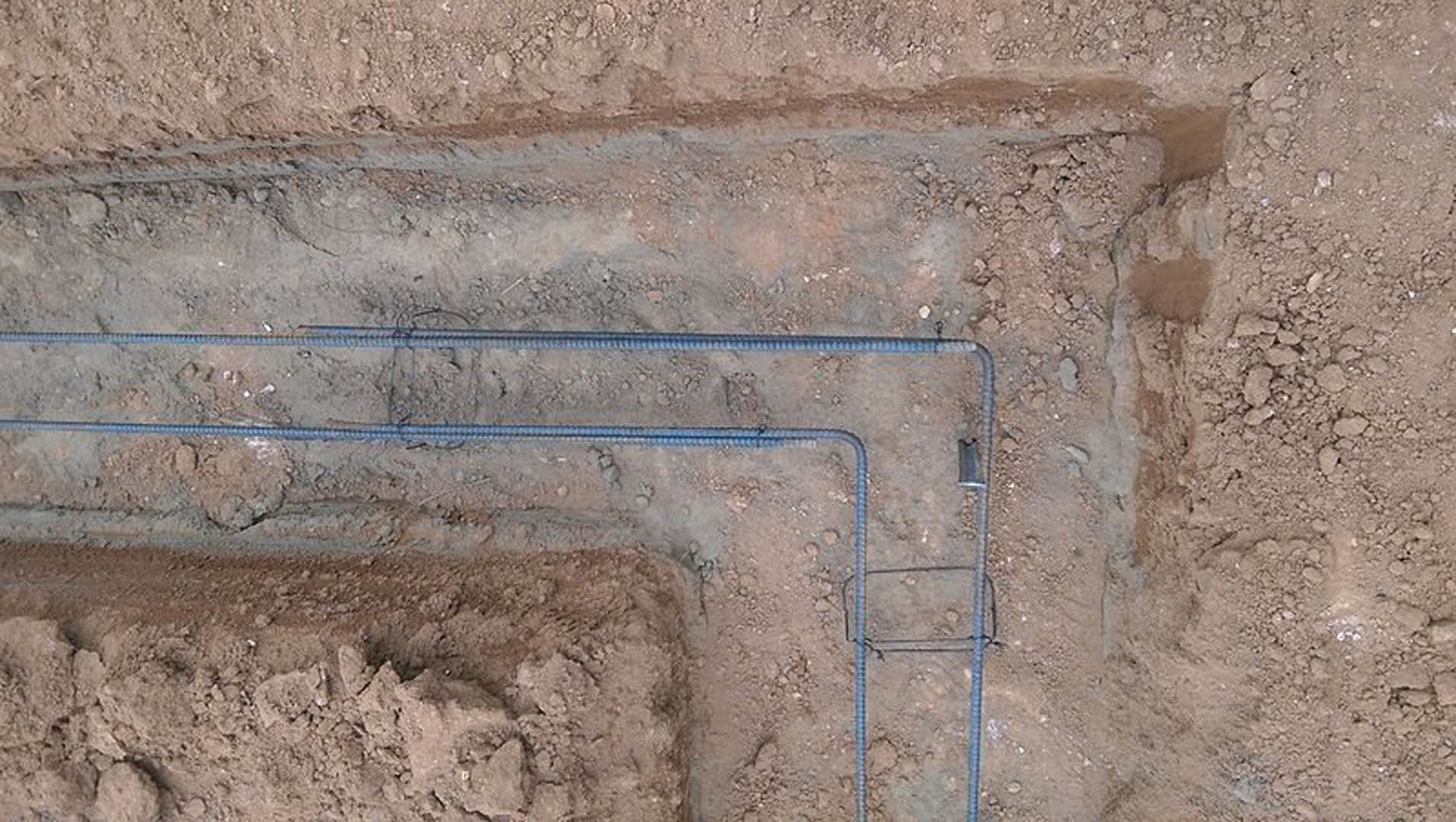 Beige pipes embedded in dirt at a residential construction site, bordered by a stone and brick wall