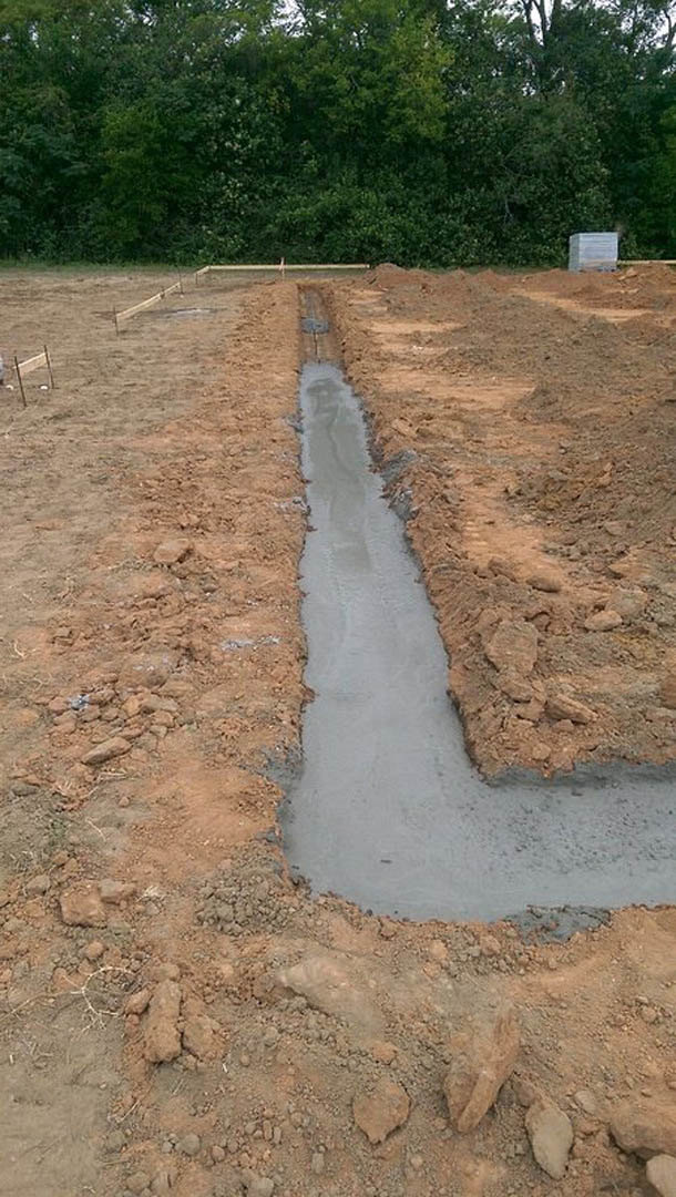 Freshly dug trench in a dirt field bordered by sparse vegetation and a wooden fence