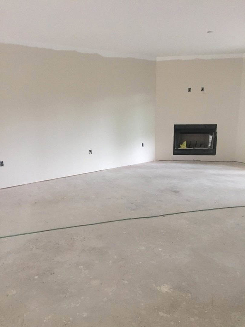Living room with smooth concrete flooring, white plaster walls, large window, and modern fireplace featuring a black surround and yellow accent inside.