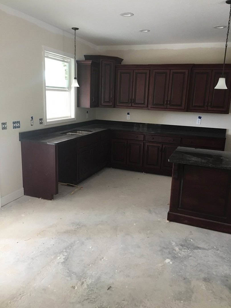 Kitchen featuring dark wood cabinets, light stone countertops, stainless steel sink beneath a window, and white pendant lamp shade