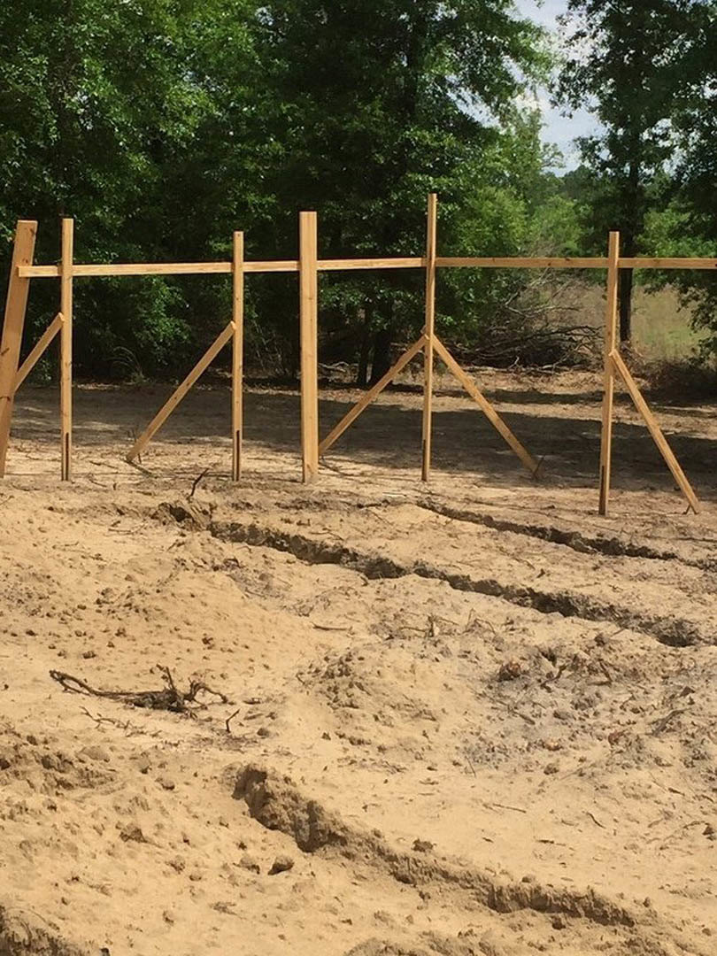 Wooden fence set in bare dirt with trees in the background