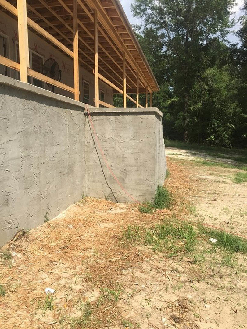 Wooden roof with exposed beams, stone and concrete walls, porch featuring red rope accent, surrounded by grass and trees.