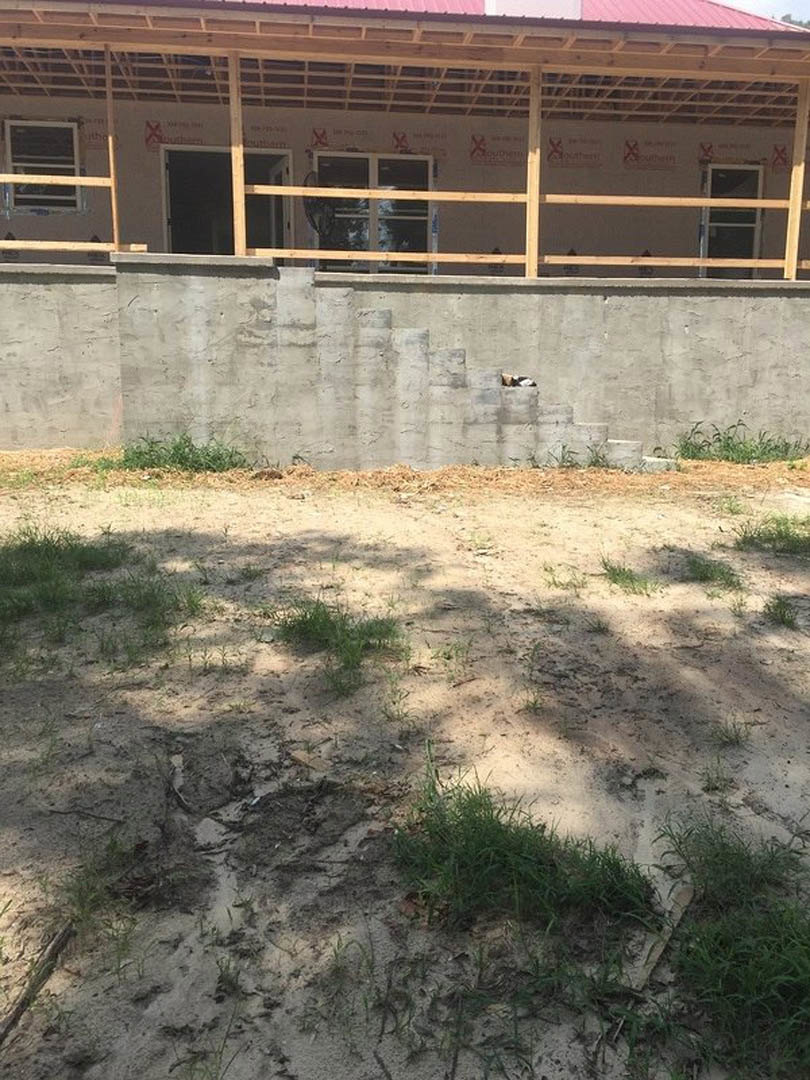 Modern house exterior with wood-framed porch, concrete wall, metal-framed window, fenced yard, and grassy lawn