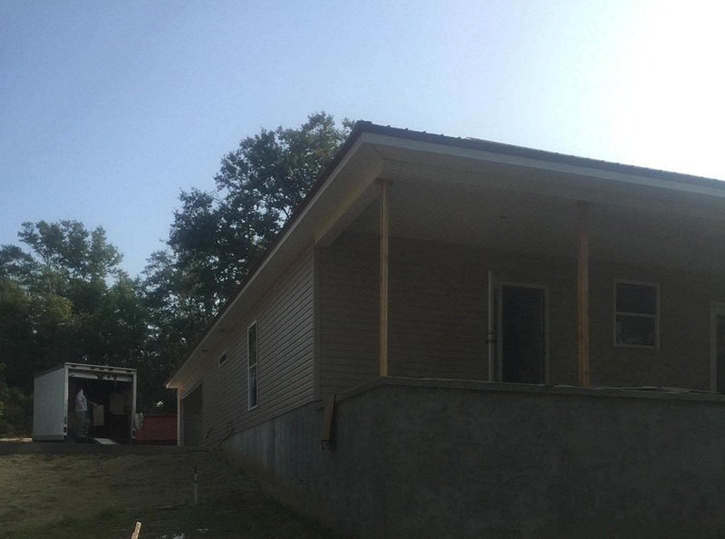 Two-story home with light siding, covered front porch, black-framed windows, concrete retaining wall, and landscaped yard with mature trees