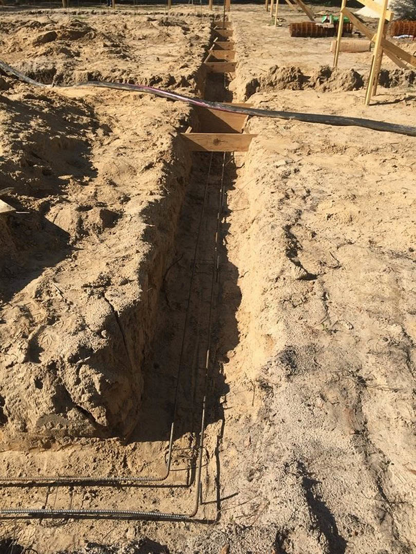 Dirt trench with exposed electrical wires running through soil outdoors