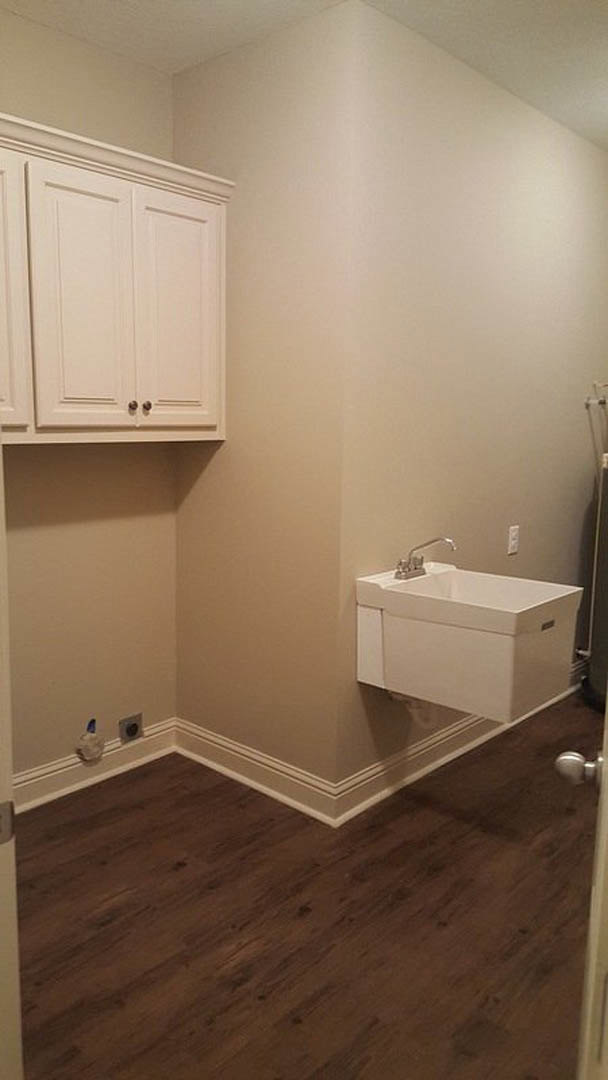 White rectangular sink with chrome faucet set against brown tile backsplash, surrounded by wood cabinetry and tiled floor.