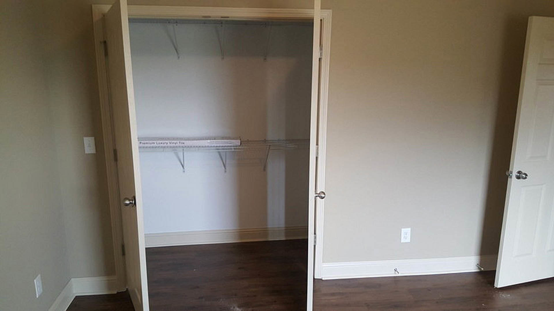 White closet with open door, built-in wood shelf, hardwood floor, white wall, and minimal decor