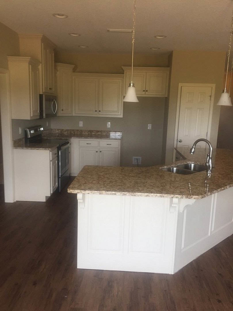 Granite kitchen countertops with tile backsplash, central island featuring sink and white pendant light, cabinetry with close-up views of drawer and door, stove integrated into