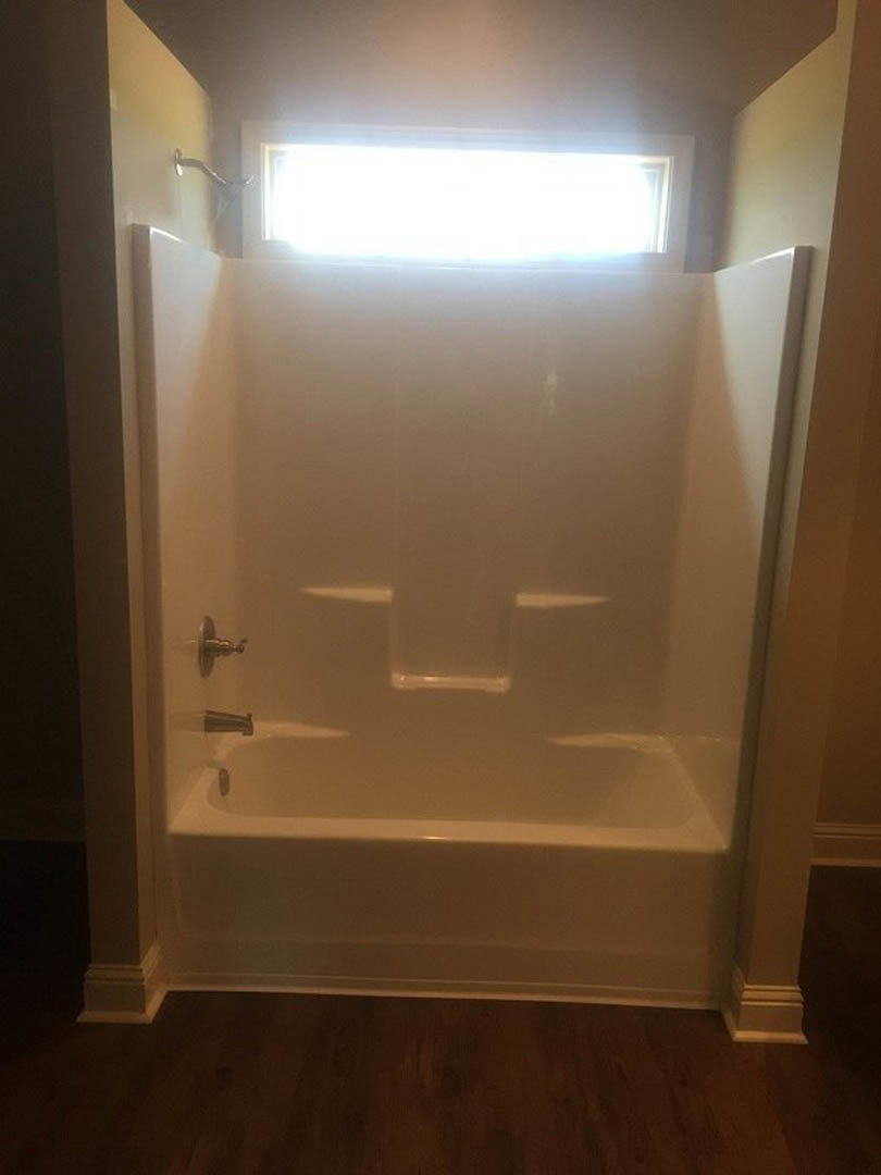Freestanding white bathtub beneath large window, surrounded by light-colored tile flooring and plaster walls, wood accent visible near tub, recessed ceiling lights overhead