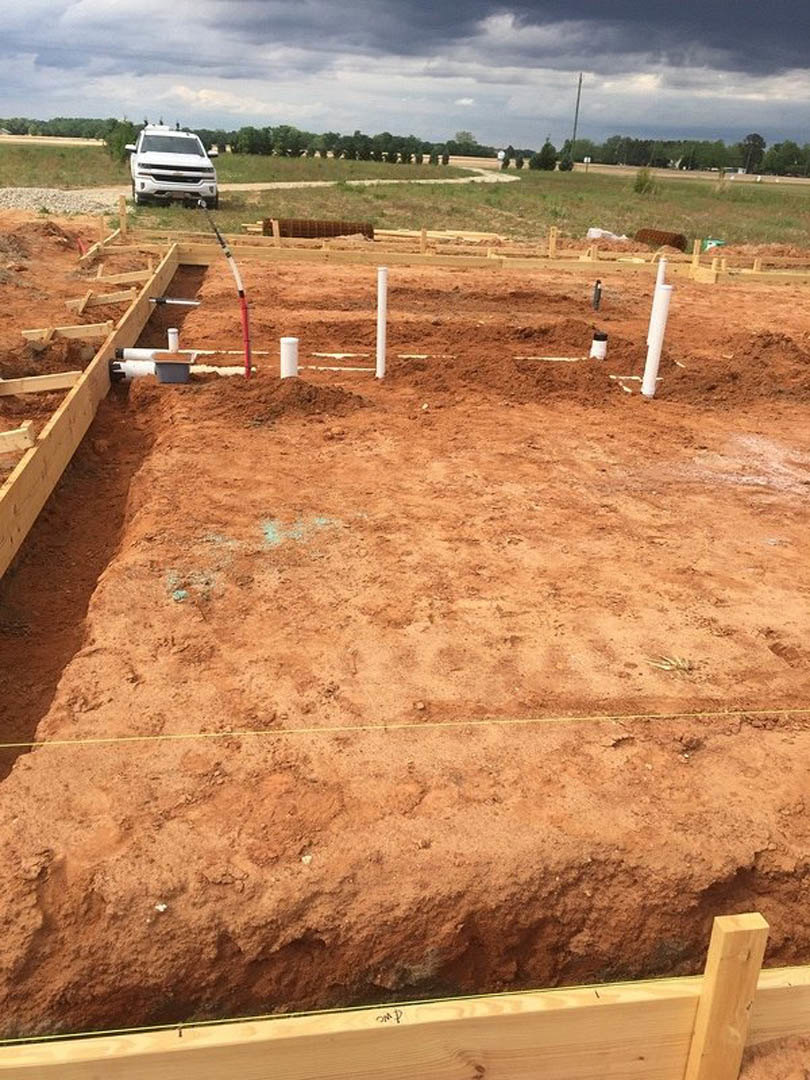 White pickup truck parked on dirt lot beside wood beams and construction fencing, cloudy sky overhead, trees in background