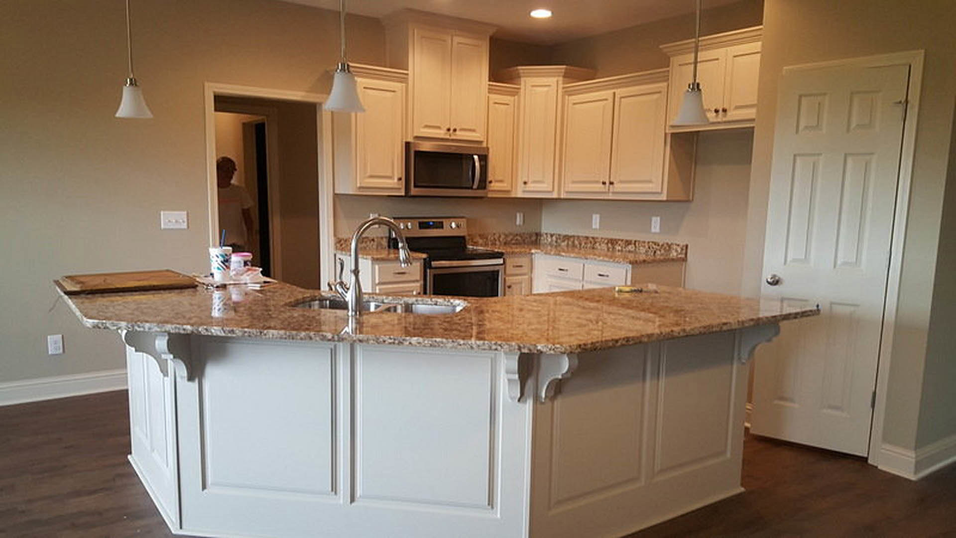 Marble kitchen island with built-in sink, white cabinetry, stainless steel microwave, and light wood flooring