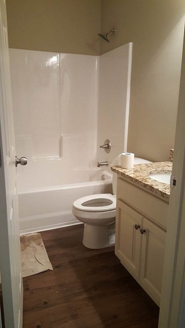 Bathroom with white toilet, built-in bathtub, tiled walls and floor, countertop with faucet, and toilet paper holder