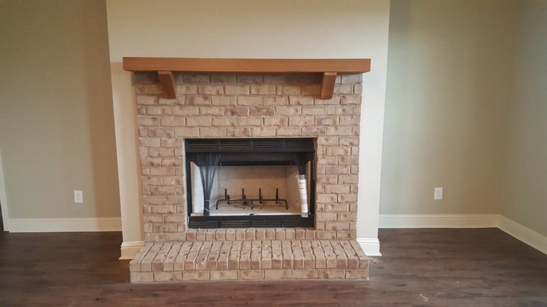 Brick fireplace with wood mantel shelf, black metal fire screen, and stone hearth in a cozy indoor living space