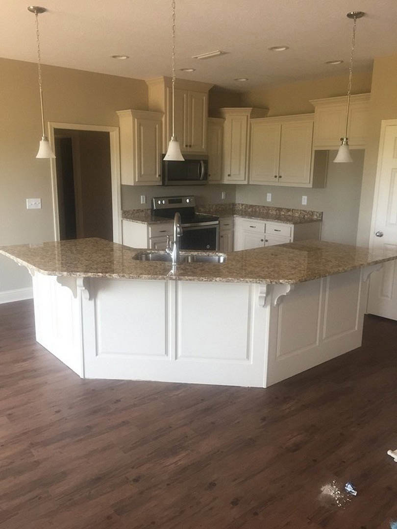 Marble kitchen island with built-in sink, white cabinetry, stainless steel stove, pendant light with white shade, and subtle white accent line on wall