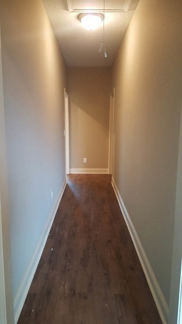 Long hallway with wood flooring, white walls, white door, ceiling light fixture, and plaster ceiling