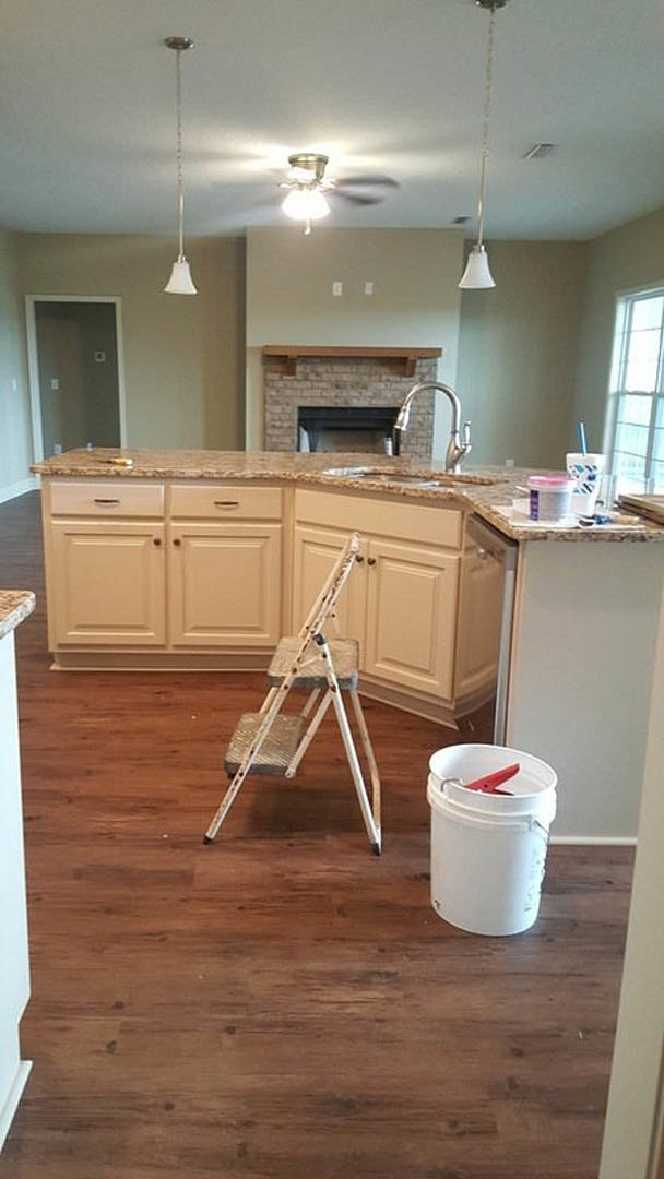 Step ladder beside white bucket with red handle on kitchen floor, sunlight streaming through window, ceiling fan and light fixture overhead, close-up of faucet, white cabinetry and