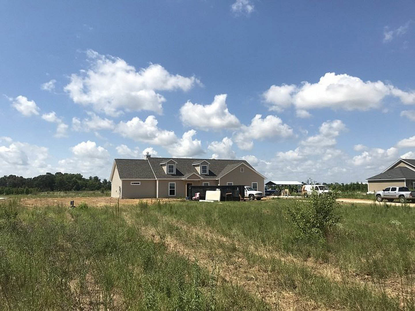 Modern farmhouse with expansive gray roof, white siding, large windows, and attached garage, set in a wide grassy field under a partly cloudy sky; white van parked near the