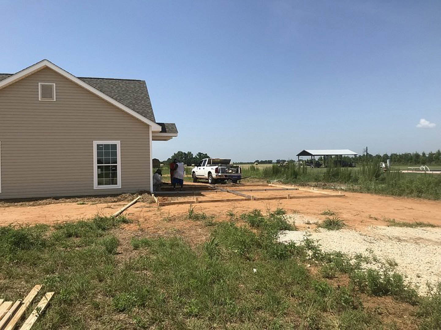 Modern house with white roof, white-framed window, exterior wall vent, and wood siding; white truck parked beside grassy lot with trees and cloudy sky in background