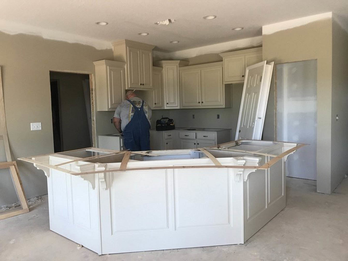 Man in white kitchen with wood-framed walls, white cabinetry, light countertops, stainless sink, and white door with doorknob