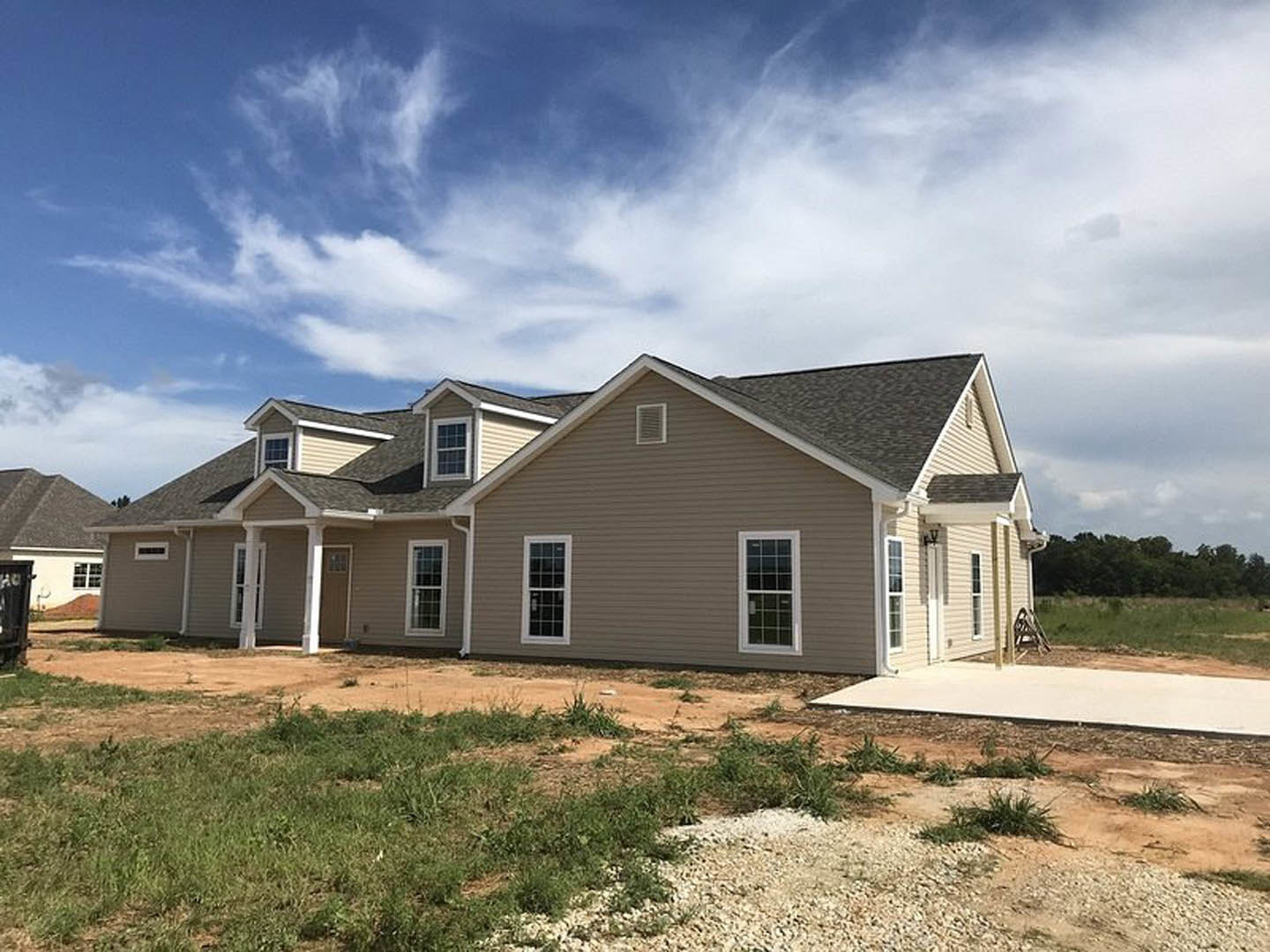 Partially built house with white framed windows, unfinished wooden siding, grassy yard, and blue sky with scattered clouds