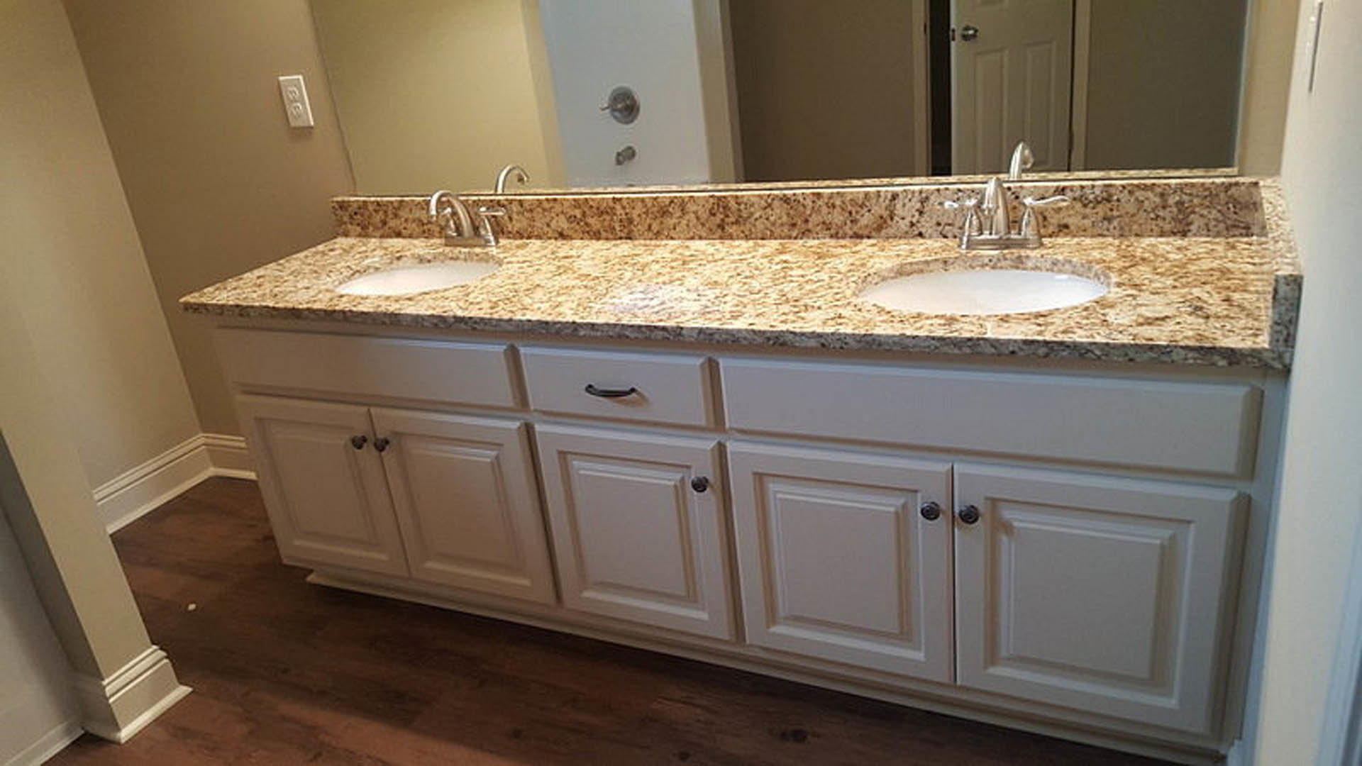 Bathroom with two undermount sinks set in a stone countertop, white cabinetry below, chrome faucets, large wall mirror, and neutral tile backsplash