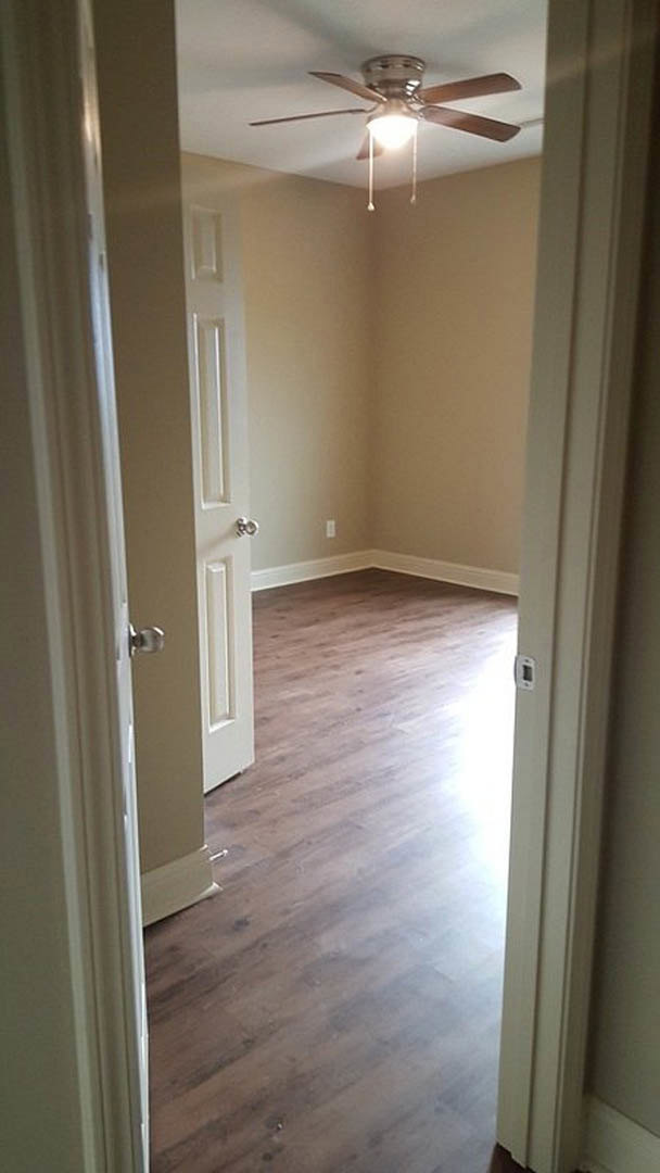 Wood flooring, white paneled door partially open, ceiling fan with light fixture, white walls with crown molding