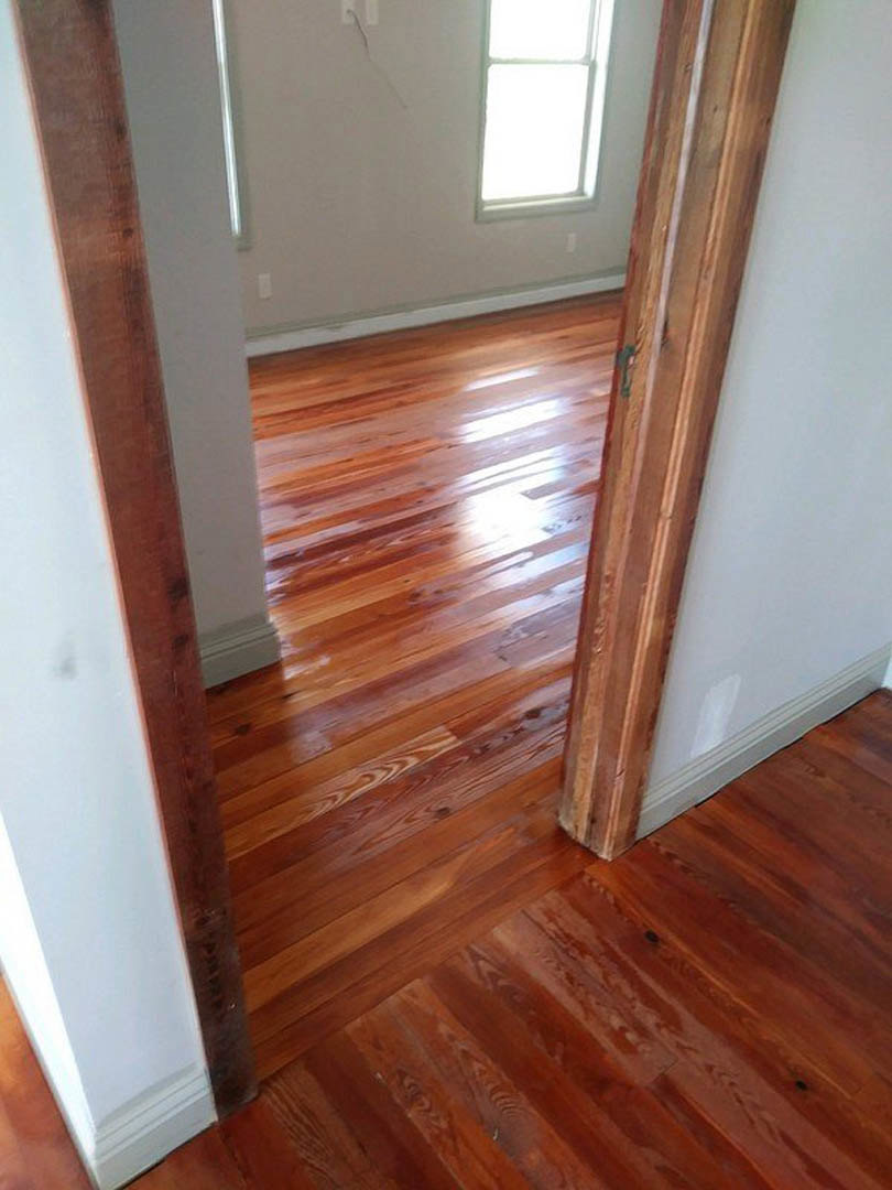 Wood plank flooring, open wooden door with white walls, sunlight streaming through window, varnished finishes