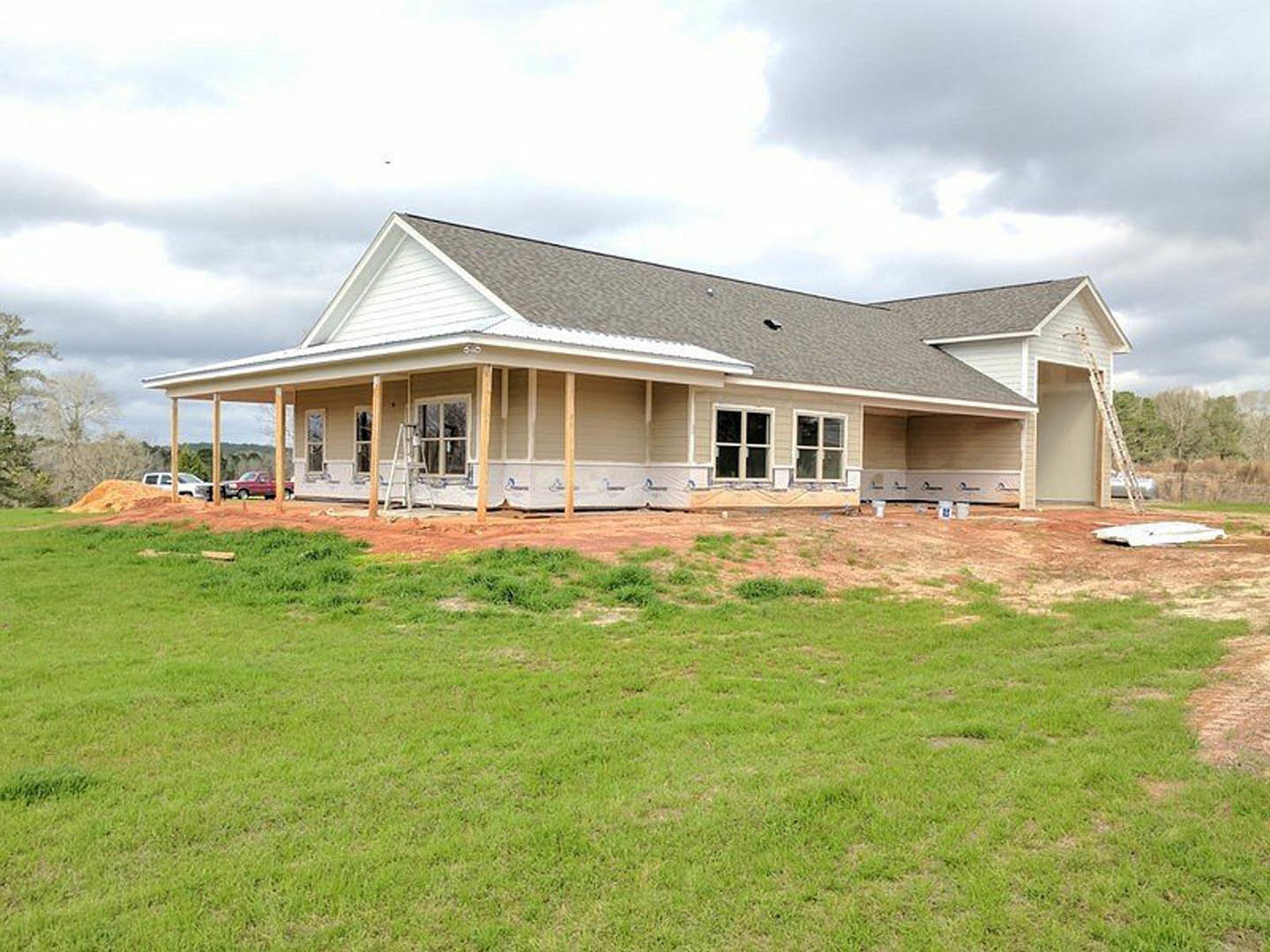 Partially built house with exposed framing and roof, surrounded by green lawn and cloudy sky