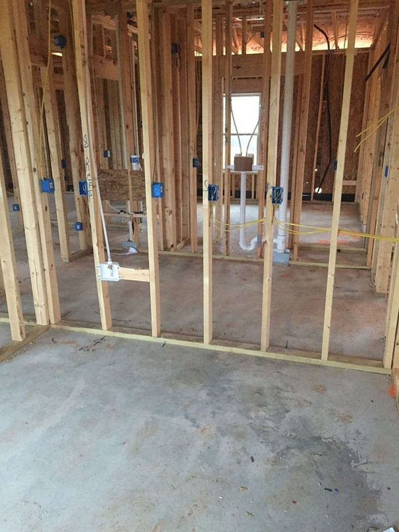 Wood-framed room under construction with exposed beams, concrete floor, window with cross muntins, white pole wrapped in yellow tape, and white container with key.