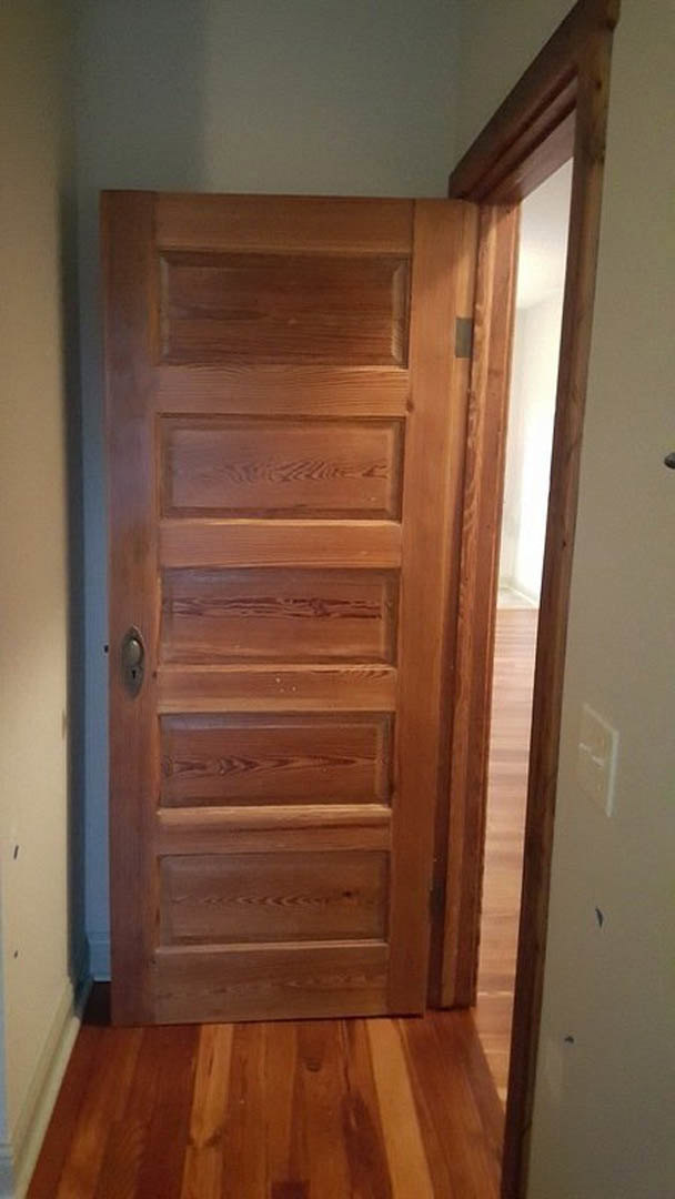 Natural wood door with visible grain, brass keyhole, and adjacent hardwood plank flooring in a neutral-toned interior room