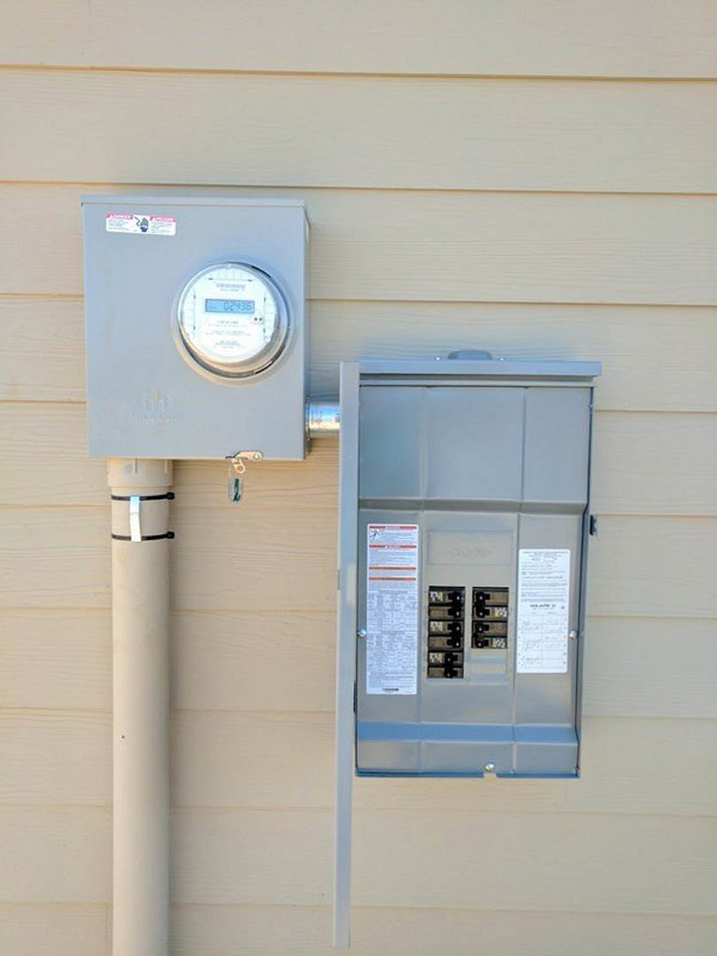 Grey electrical meter box mounted on exterior wall with digital display and black handle