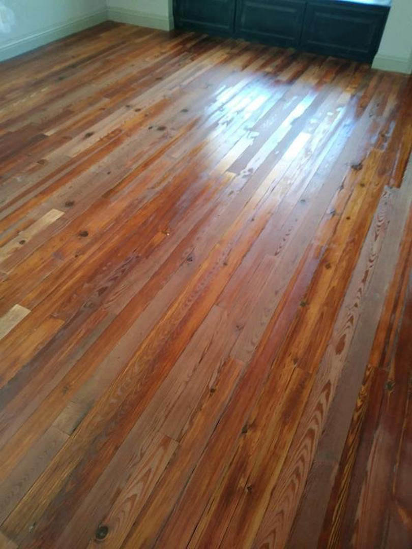 Wide-plank hardwood floor with natural finish, white painted walls, sunlight streaming across flooring, blue cabinet in background, close-up detail of wood grain and white accent