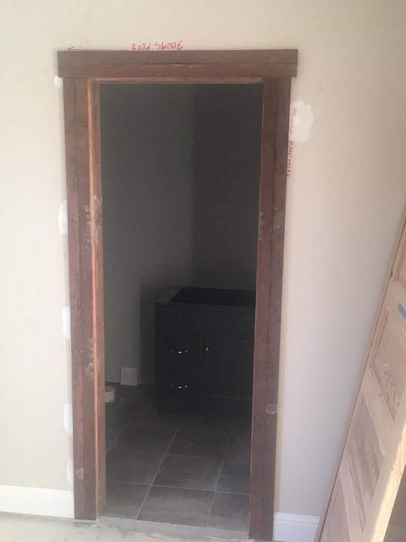 Wooden door set in a white wall, black cabinet with silver handles, grey tile flooring